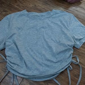 grey crop top with adjustable strings on both sides of the shirt.